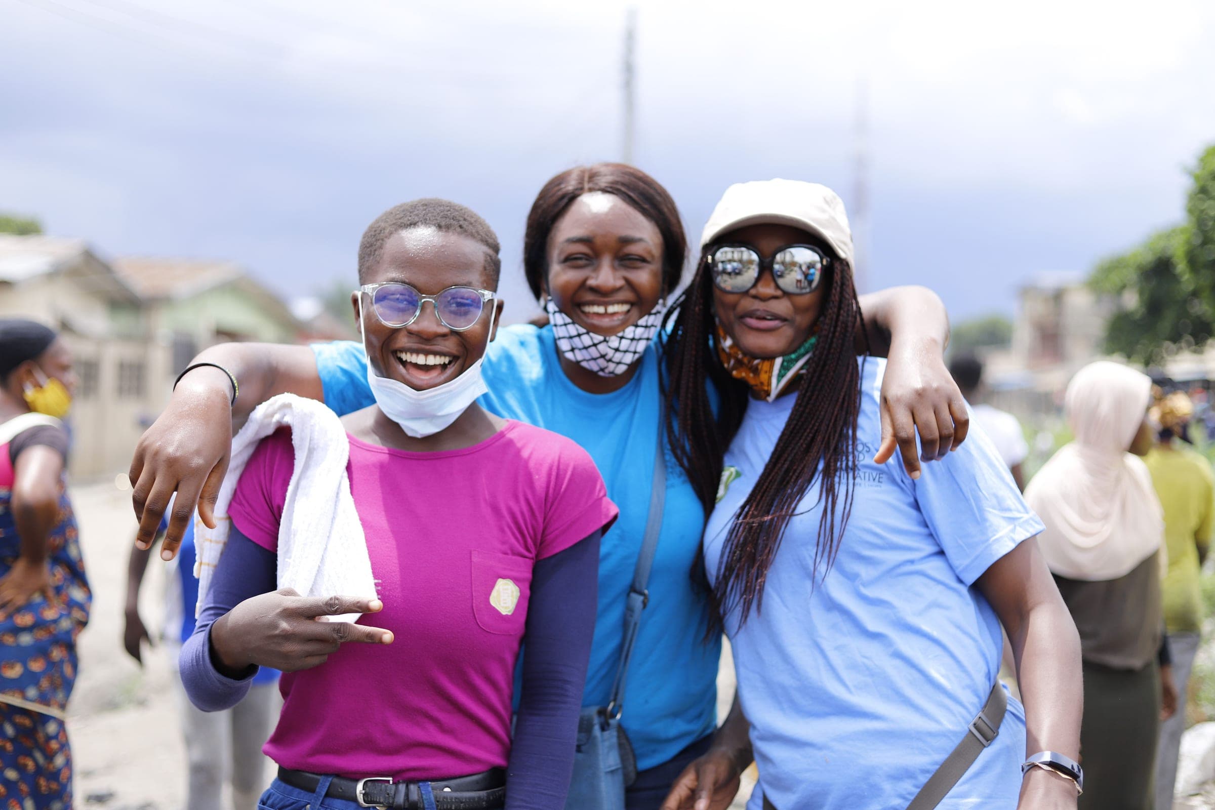 Three smiling volunteers standing arm in arm at a community outreach day
